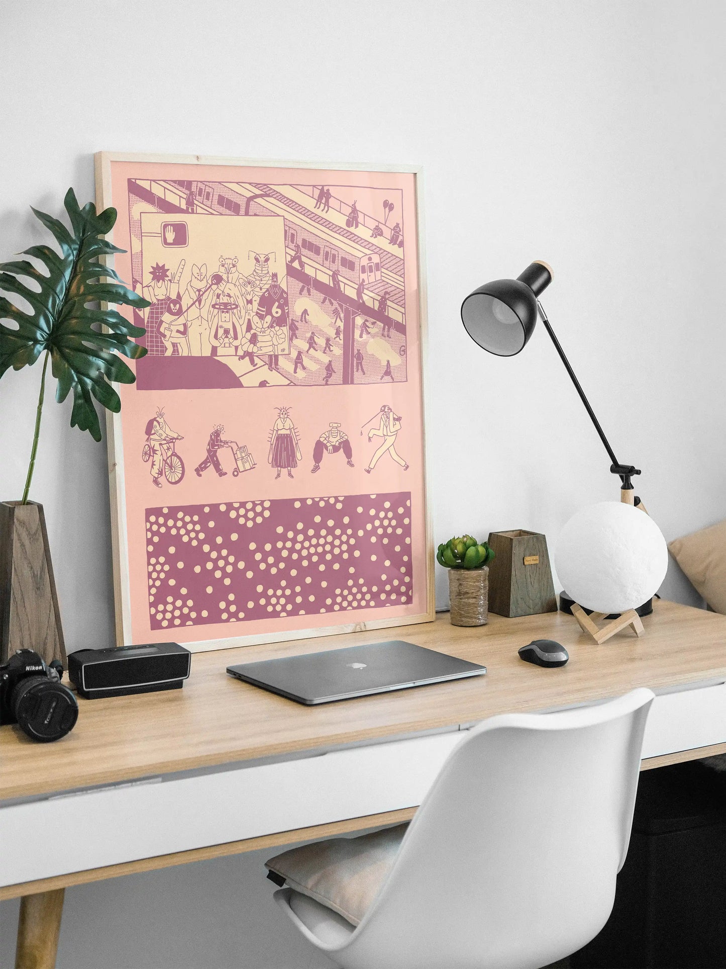 Framed “Bug Vision” city illustration poster by NYC artist Max Kolo displayed on a modern white desk setup, featuring stylized insect characters commuting through a bustling urban scene in bold pink and purple panels.