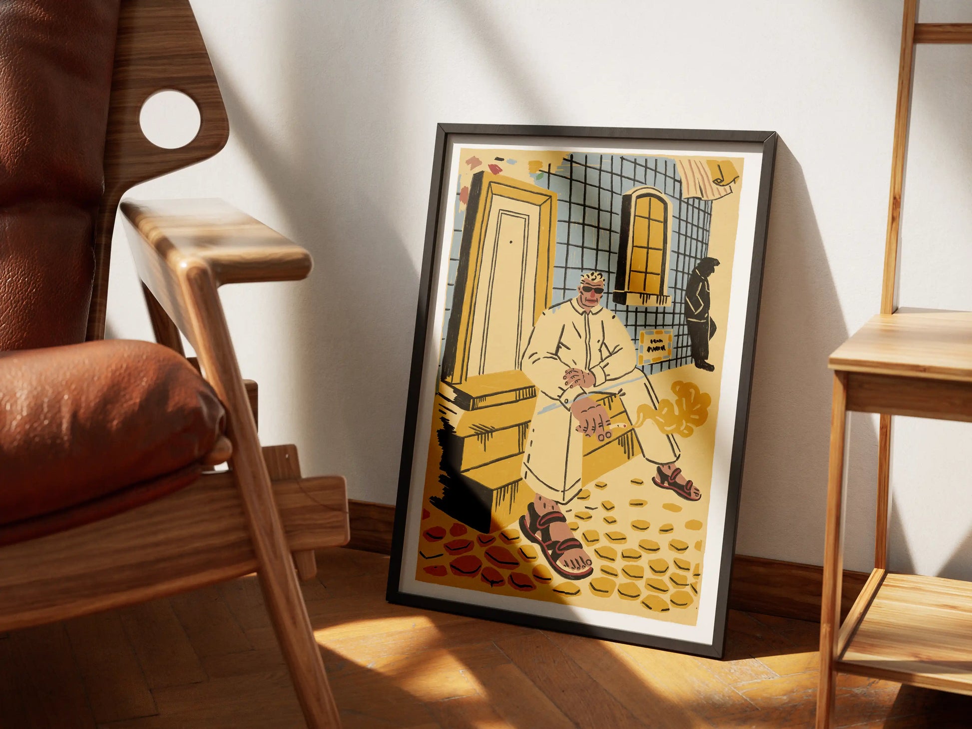 Framed ‘Lisbon’ city illustration poster by NYC artist Max Kolo resting on a wooden floor between mid-century modern style chairs, featuring a stylized Lisbon man sitting on tiled steps in warm yellow and blue tones.