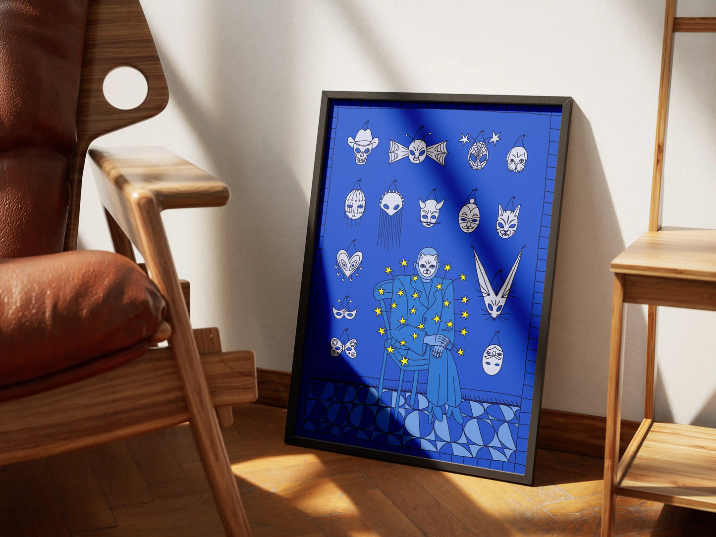 Framed Mask Salesman art print by Max Kolo leaning against a wall in a bright room with wooden furniture, featuring a surreal blue design with expressive floating masks.