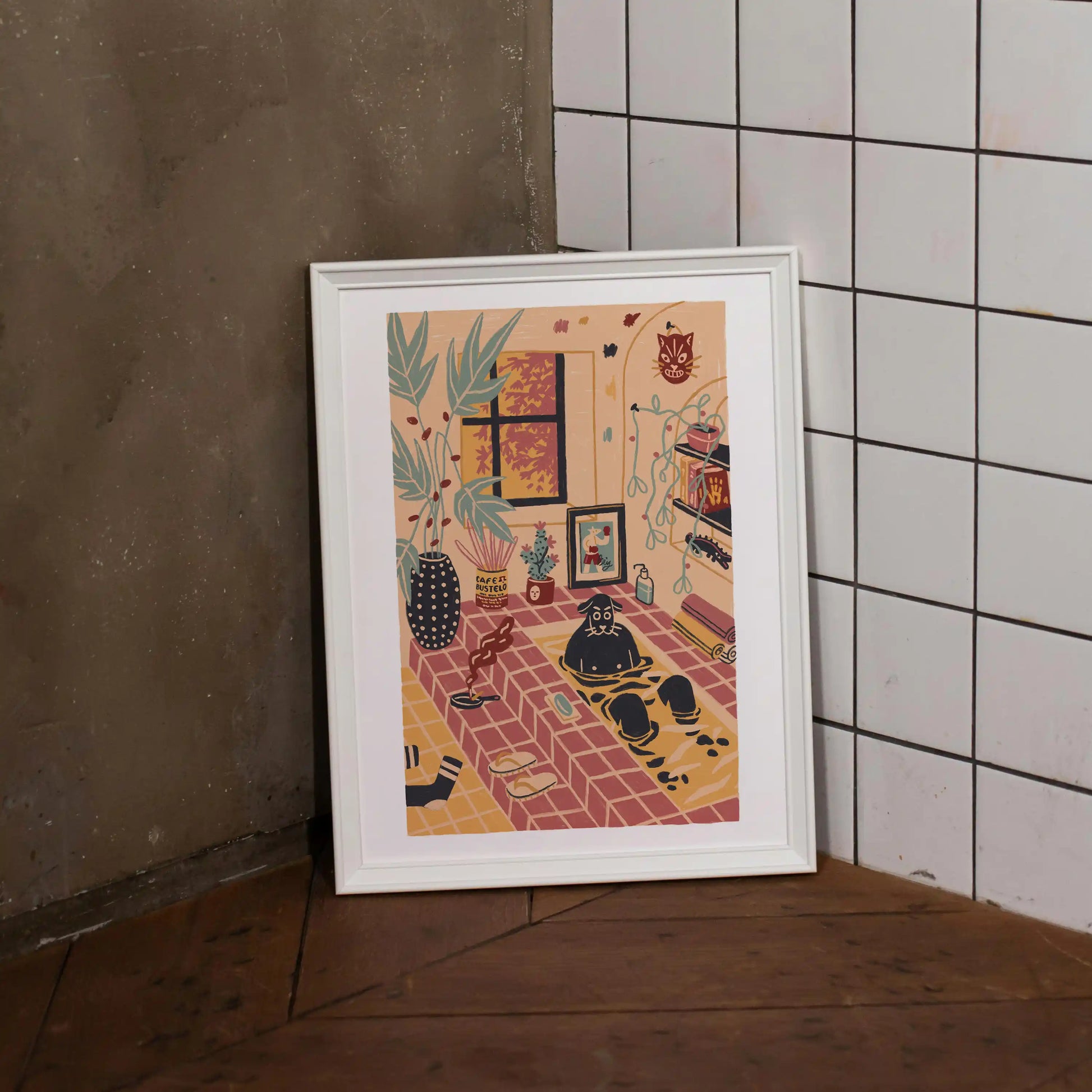 Framed “Me Time” art print by Max Kolo, featuring a cozy illustrated room with plants, warm tile flooring, a window, shelves, and a relaxed black dog, displayed leaning against a textured concrete wall beside white square tiles on a wooden floor.