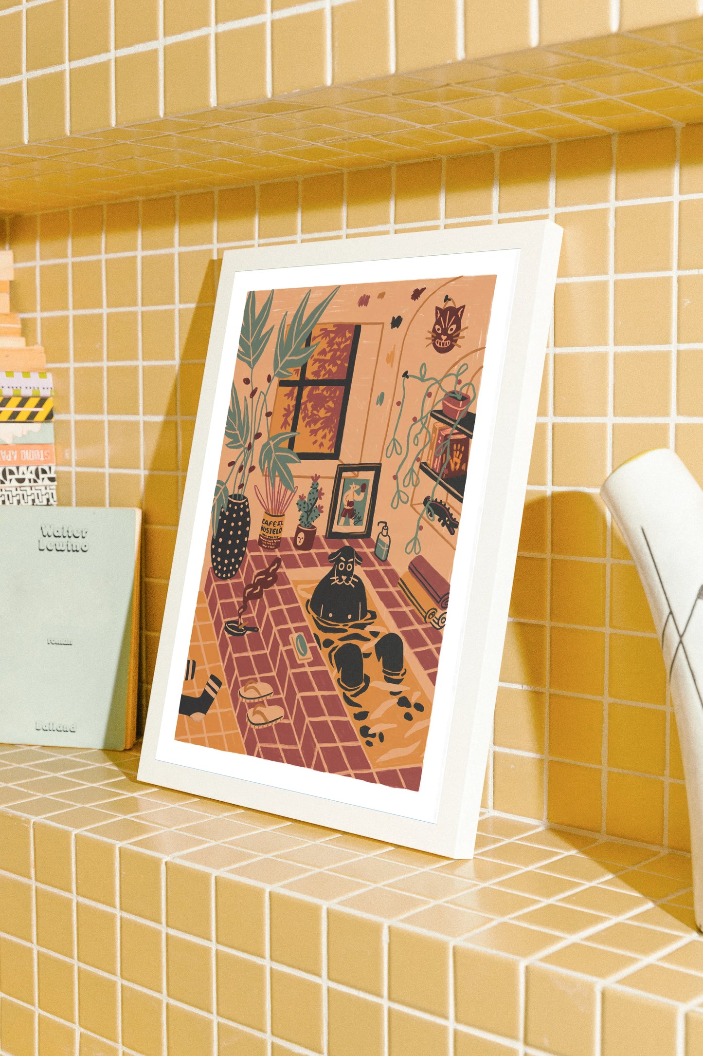 Framed artwork on a tiled shelf with a yellow-tiled wall background. Framed artwork by New York City (NYC) based artist Max Kolo of an illustration of a dog having a bath, taking some alone time. 