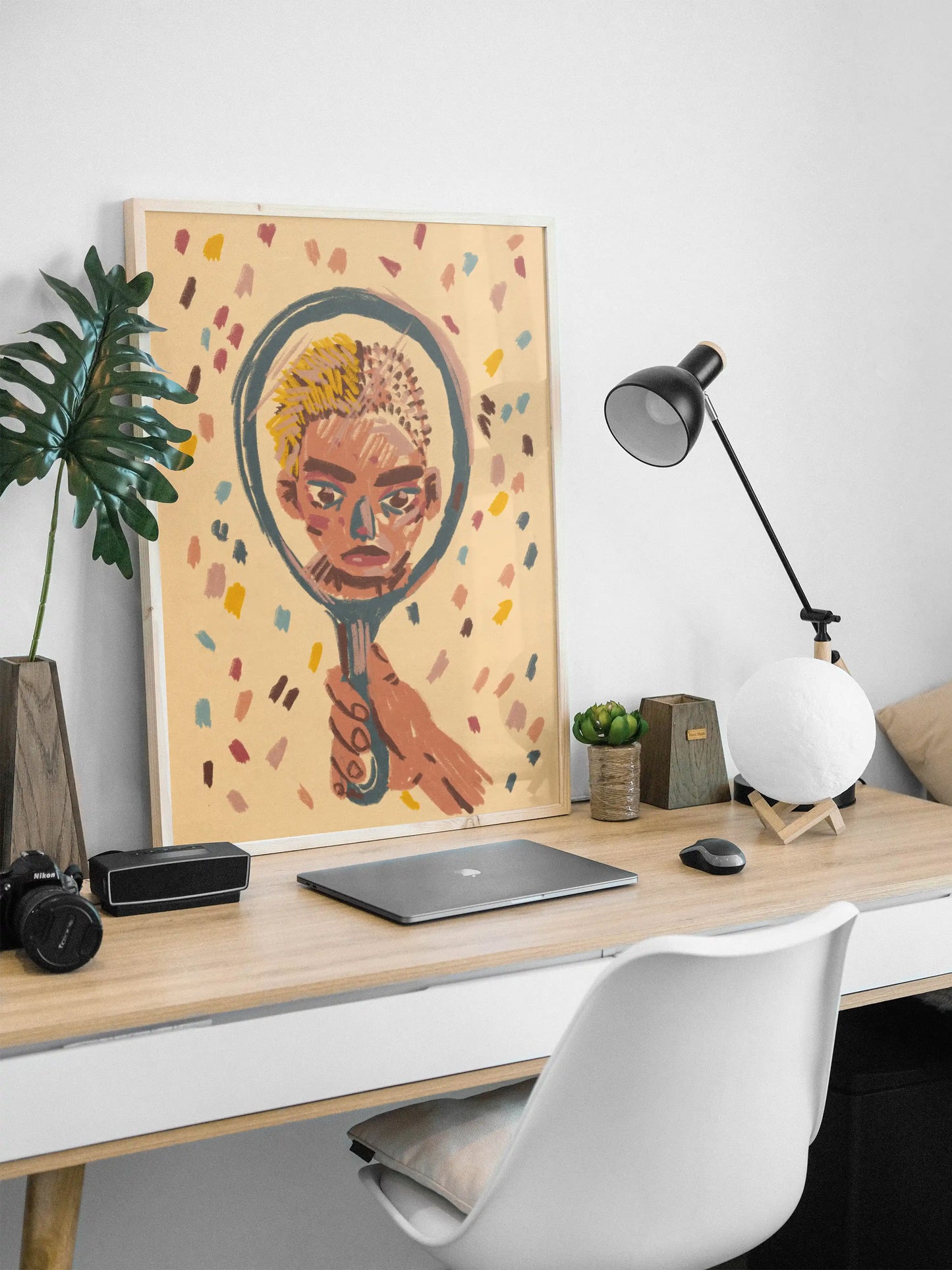 Framed ‘Mirror’ poster by NYC artist Max Kolo displayed on a modern minimalist desk with laptop, lamp, and plants, featuring a stylized face reflected in a hand-held mirror illustration.
