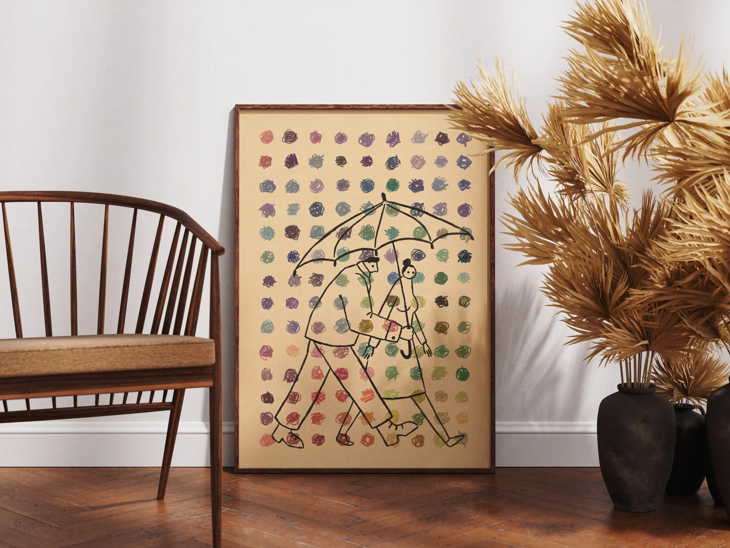 Framed illustration by NYC artist Max Kolo depicting two stylized figures walking together under a single umbrella as colorful rain falls, displayed on a wooden floor beside a mid-century chair, dried decorative plants, and ceramic vases.